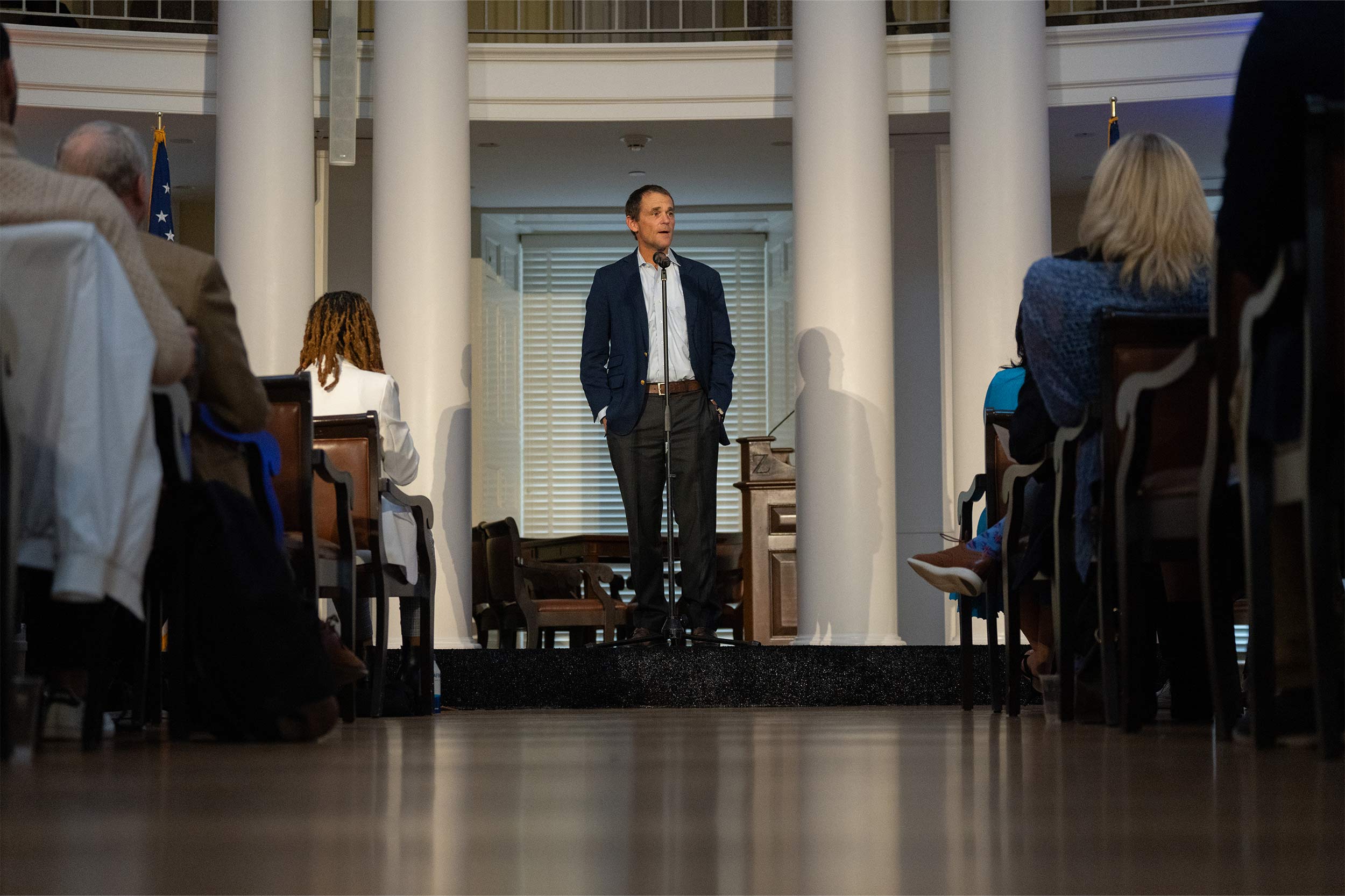 UVA President Jim Ryan stands in front of a seated crowd, speaking at a standing microphone.