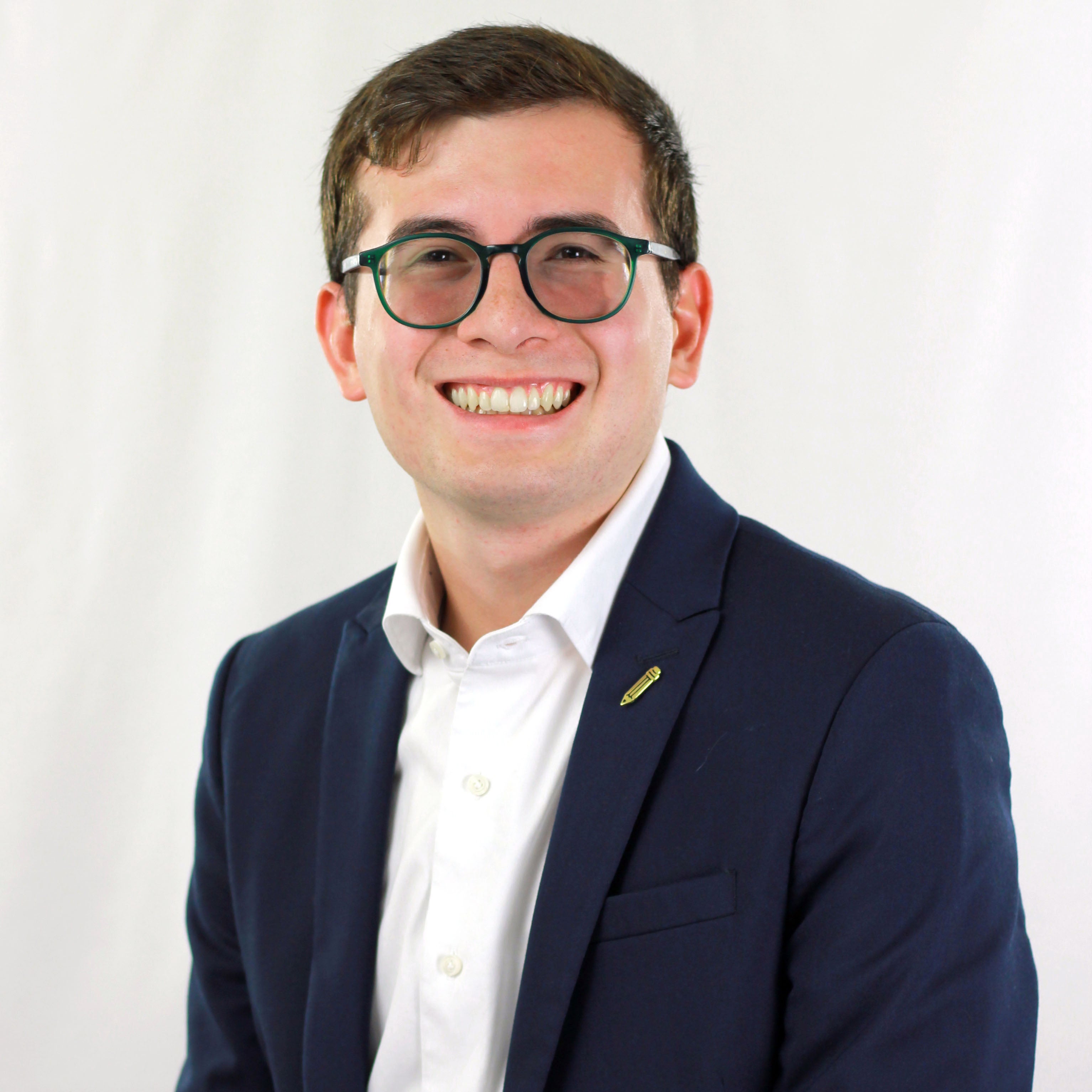 Portrait of smiling young man wearing glasses, blue jacket, white shirt, against a plain white background