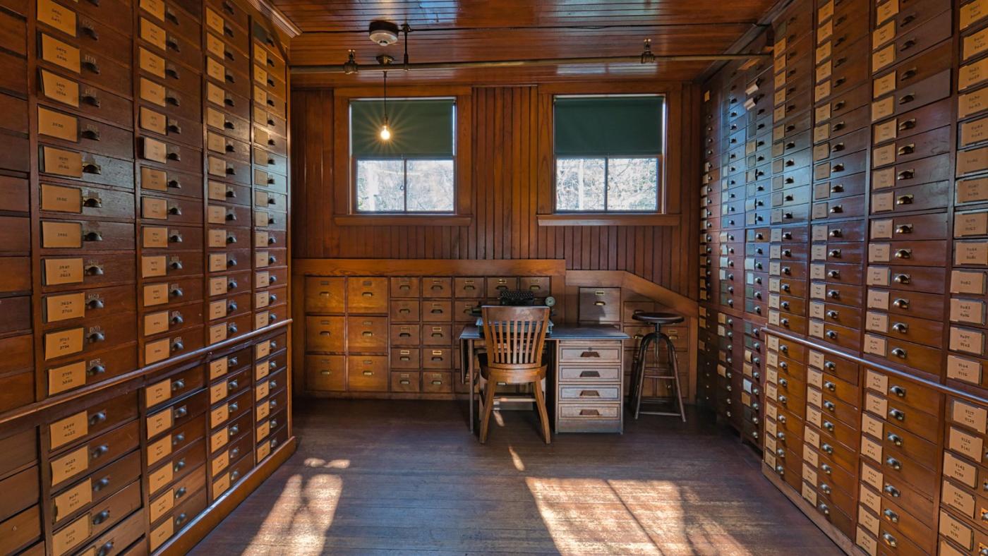 Olmsted firm - Many wooden boxes line both sides of wall in wooden room, with a desk and chair on the far end