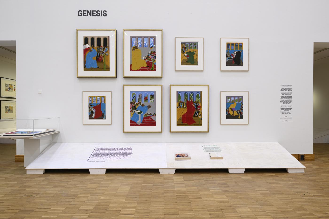 Grid of 8 paintings on wall with a shelf on floor with text and books.